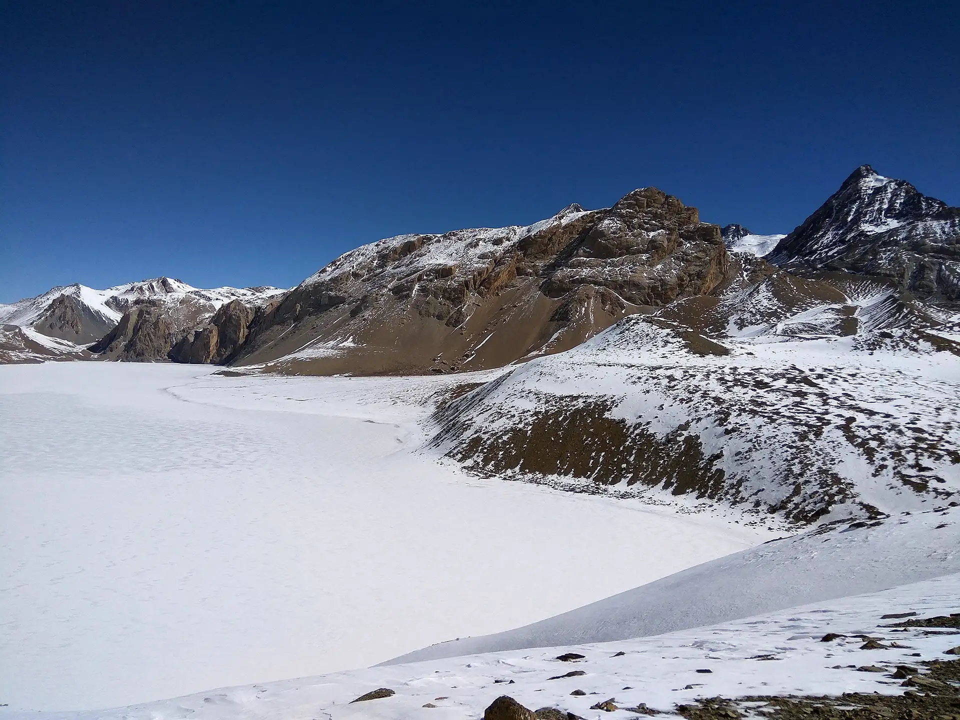 The frozen, turquoise surface of Tilicho Lake surrounded by massive snowy peaks.
